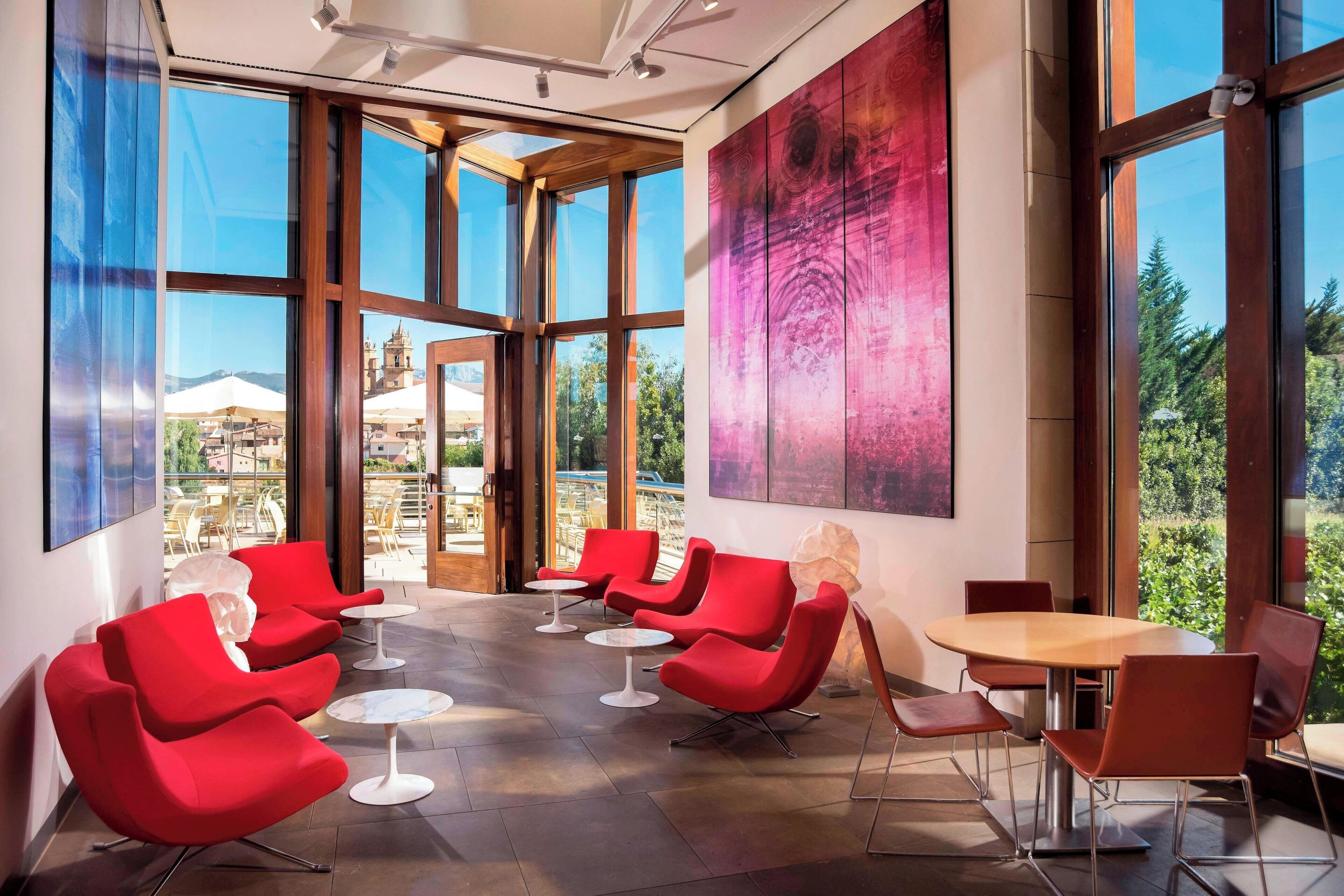 Un interior moderno con amplias ventanas, sillas rojas y una mesa de madera.