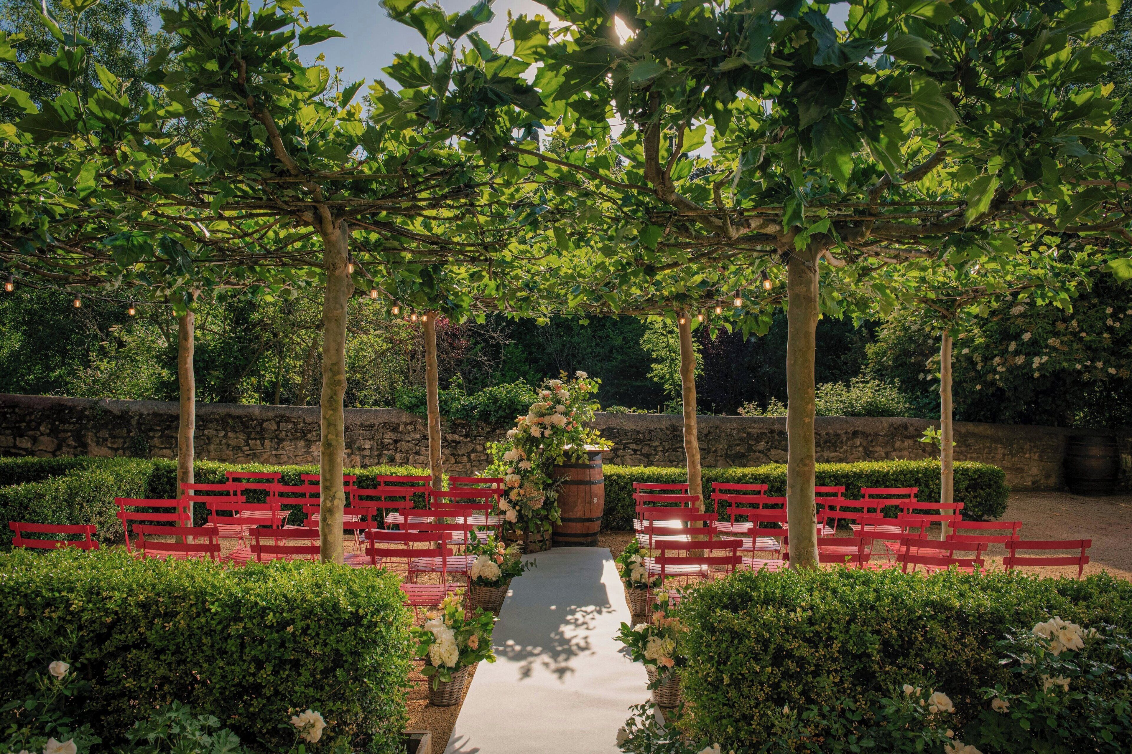 A garden setting with a pathway lined by red benches and a central floral arrangement.