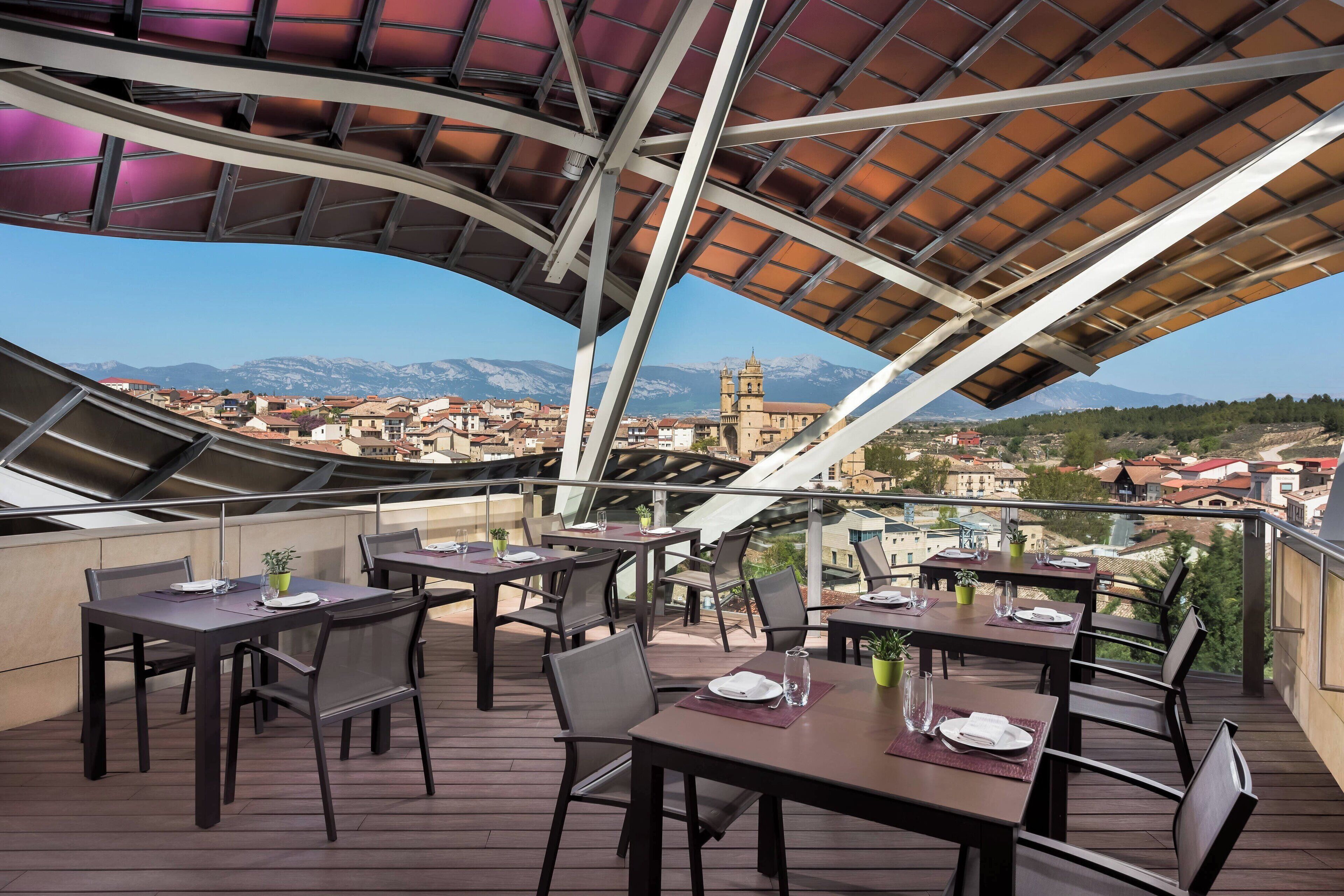 An outdoor dining area with tables and chairs, overlooking a mountainous landscape and a historic building.