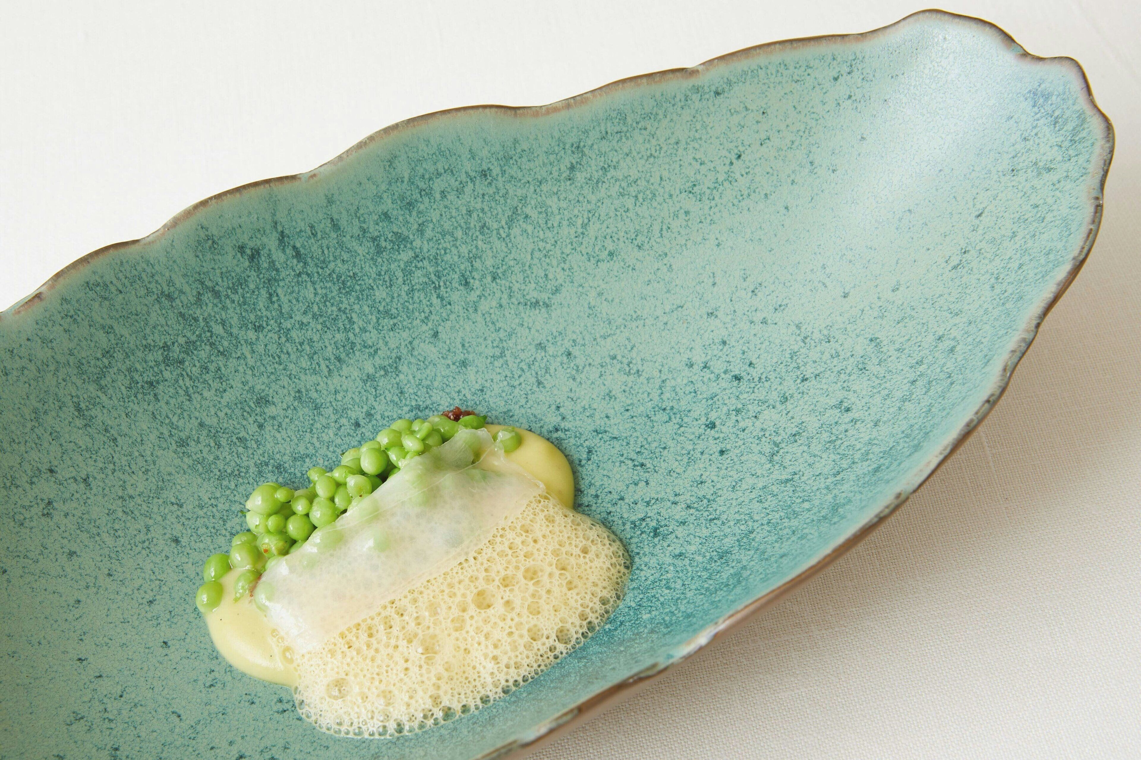 Un plato de cerámica con un tono verdoso, que contiene una sustancia blanca y guisantes verdes.