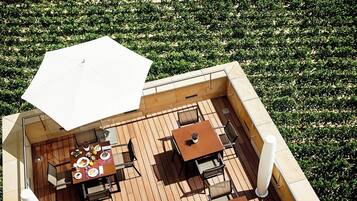 Una terraza exterior con piso de madera, una mesa con sillas y un paraguas grande.