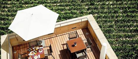 Una terraza exterior con piso de madera, una mesa con sillas y un paraguas grande.