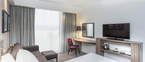 Moderni hotellihuone, jossa on suuri sänky, työpöytä, jossa on televisio, tuoli ja näkymä ulos.