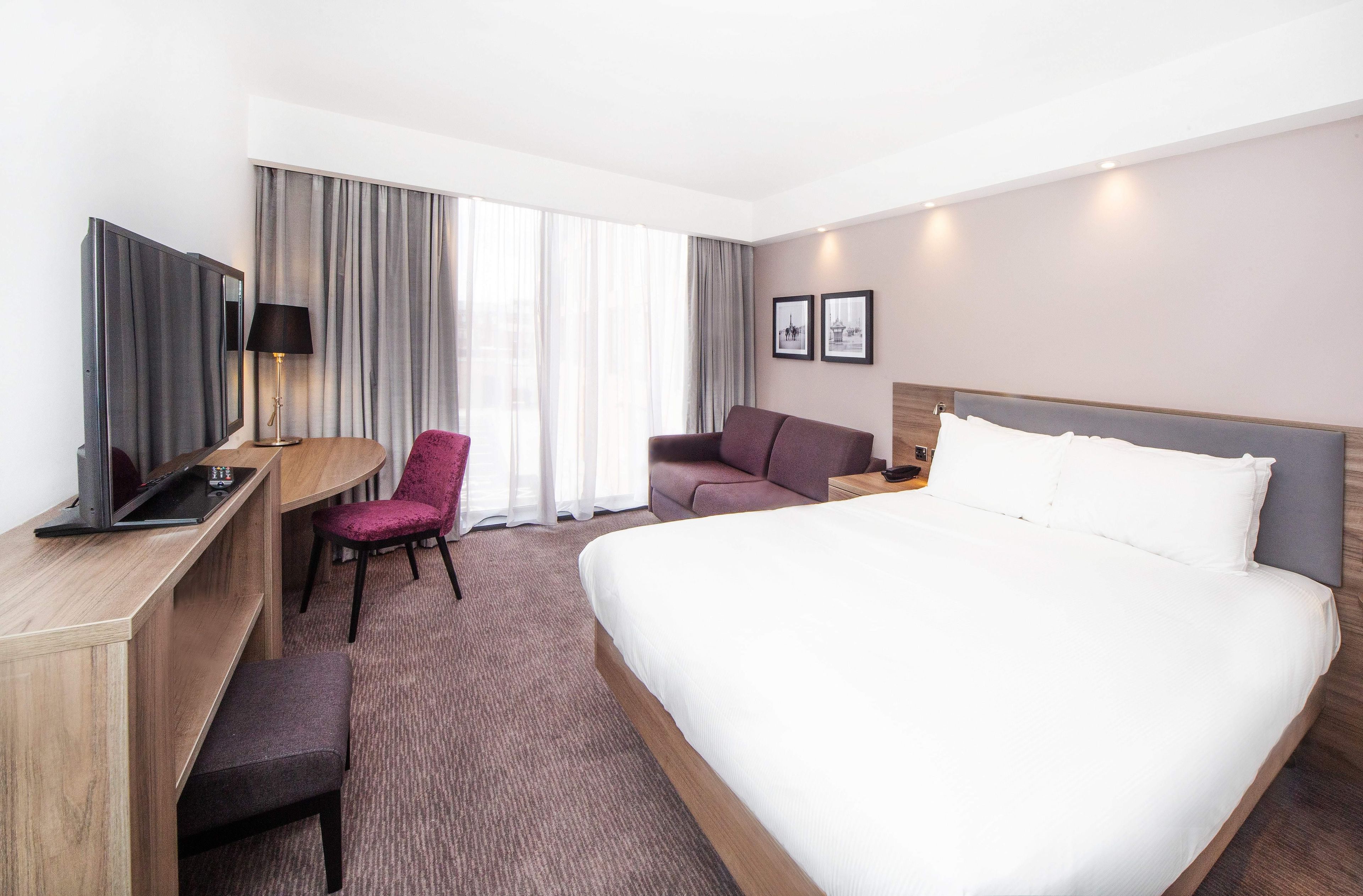 Ein Hotelzimmer mit einem großen Bett, einem Schreibtisch mit Computer, einem Sessel und einer Couch.