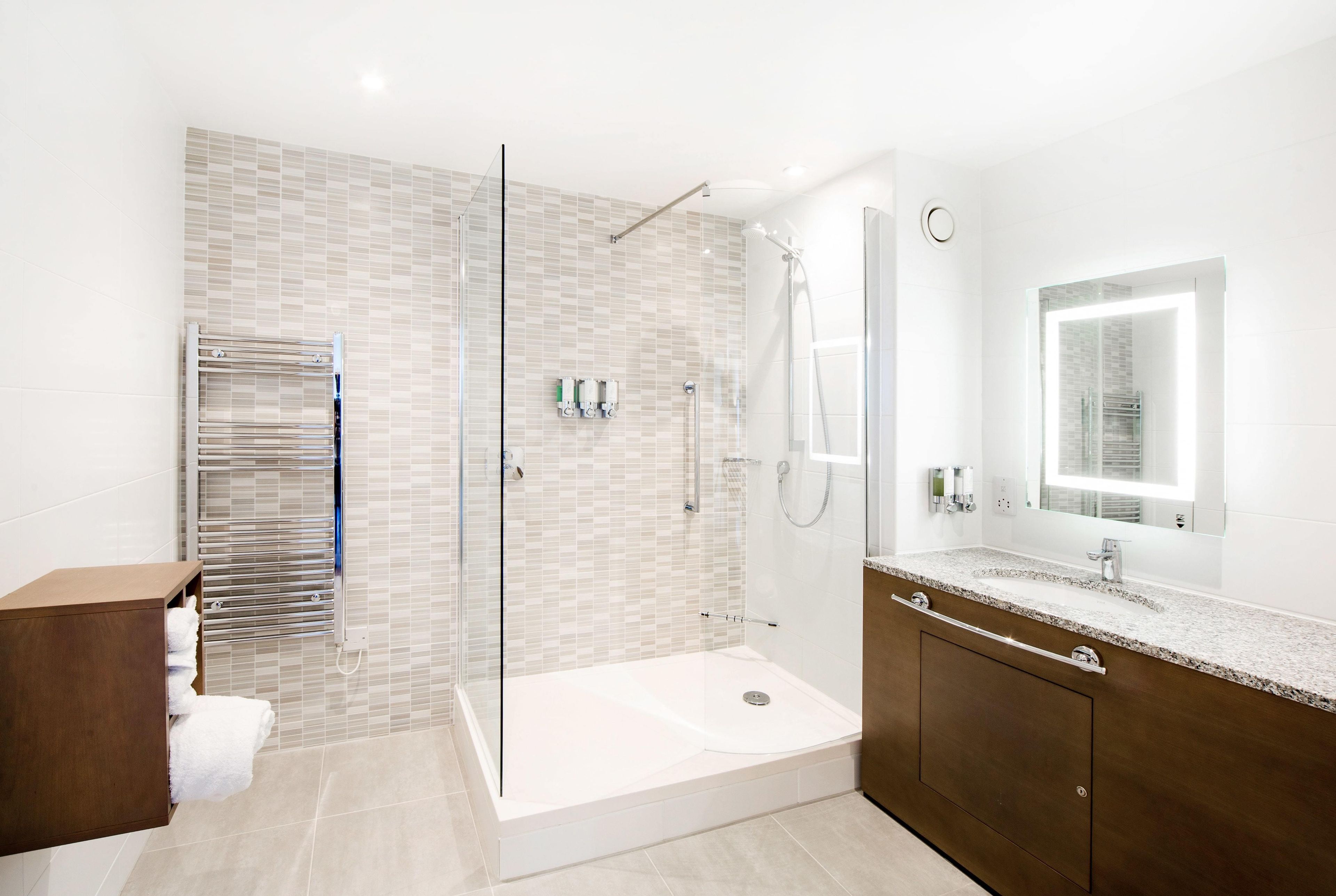 A modern bathroom with a glass-enclosed shower, a vanity with a mirror, and a towel rack.