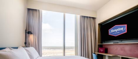 Une chambre d’hôtel avec un grand lit, un téléviseur fixé au mur et une vue sur la plage.
