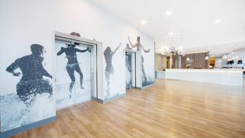 Een ruime hotel lobby met een houten vloer, een receptiebalie en wanddecoraties met afbeeldingen van bewegende mensen.