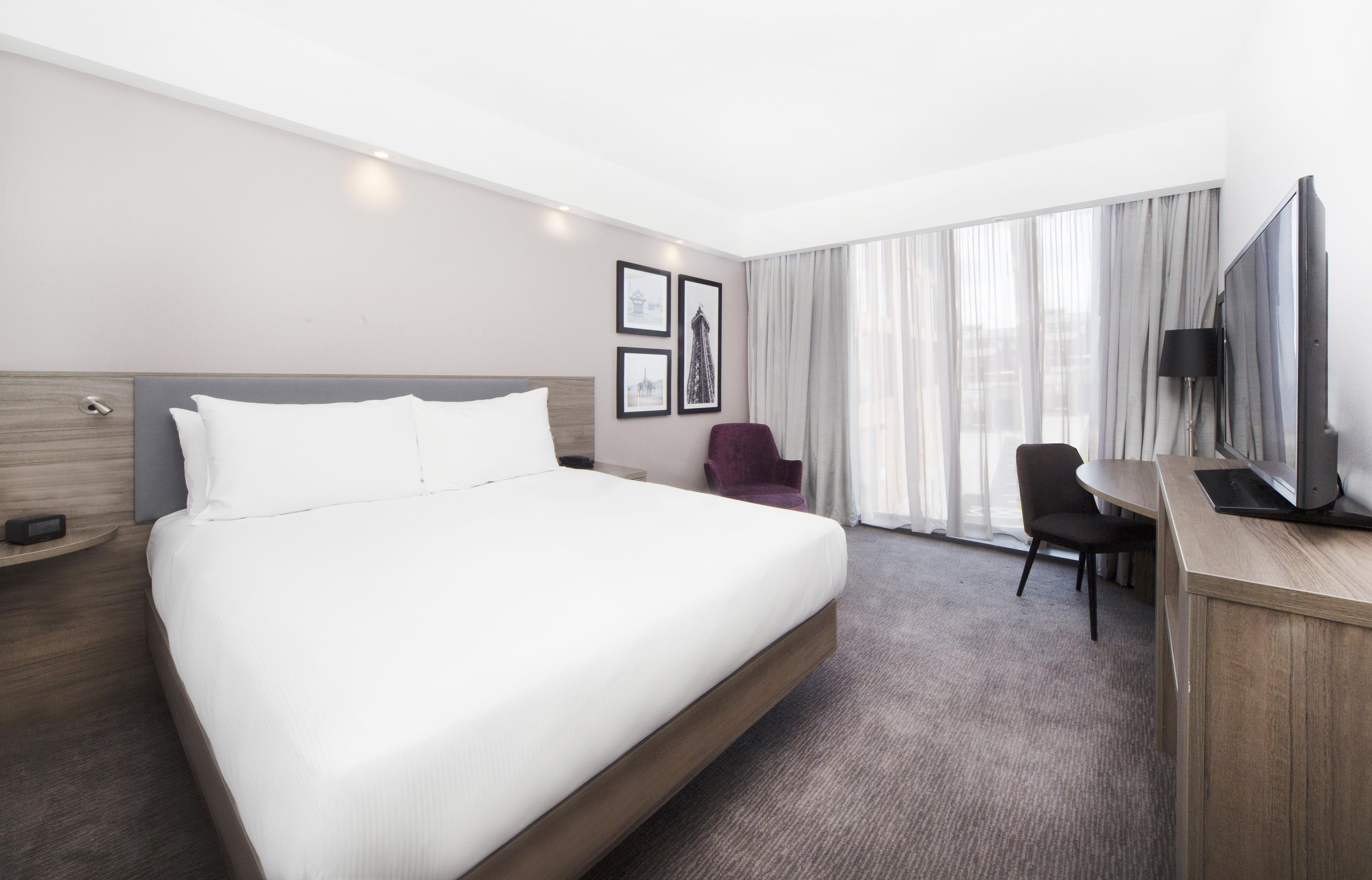 A hotel room with a large bed, a desk, a chair, a television, and a window with curtains.