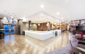 A spacious hotel lobby with a central reception desk, seating area, and a view of the parking garage.
