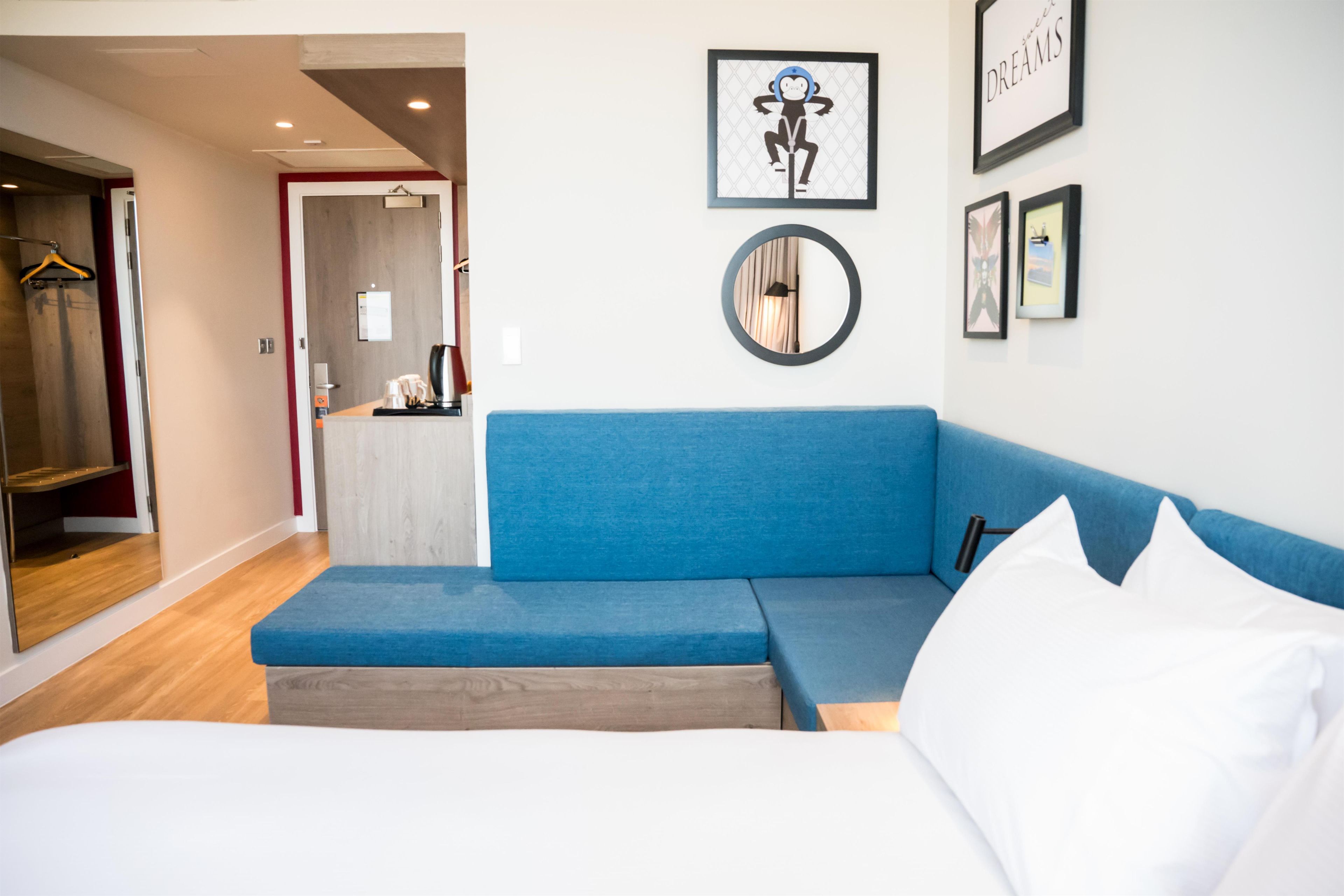 A hotel room with a bed, a blue sofa, a round mirror, and artwork on the walls.