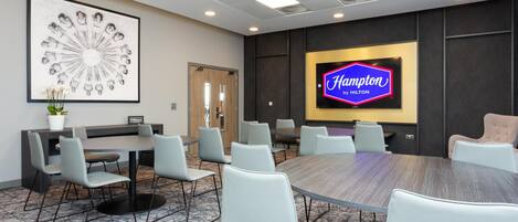 A conference room with a large table, chairs, a framed artwork, a television screen, and a door.