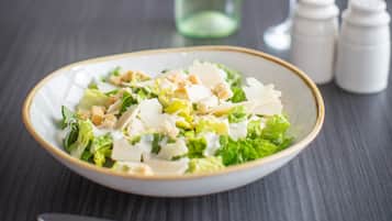 Uma salada com croutons e queijo, uma garrafa de vinho branco e dois saleiros e pimenteiros sobre uma mesa de madeira escura.