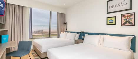 Habitación de hotel con dos camas, un escritorio, una silla y vistas al exterior.