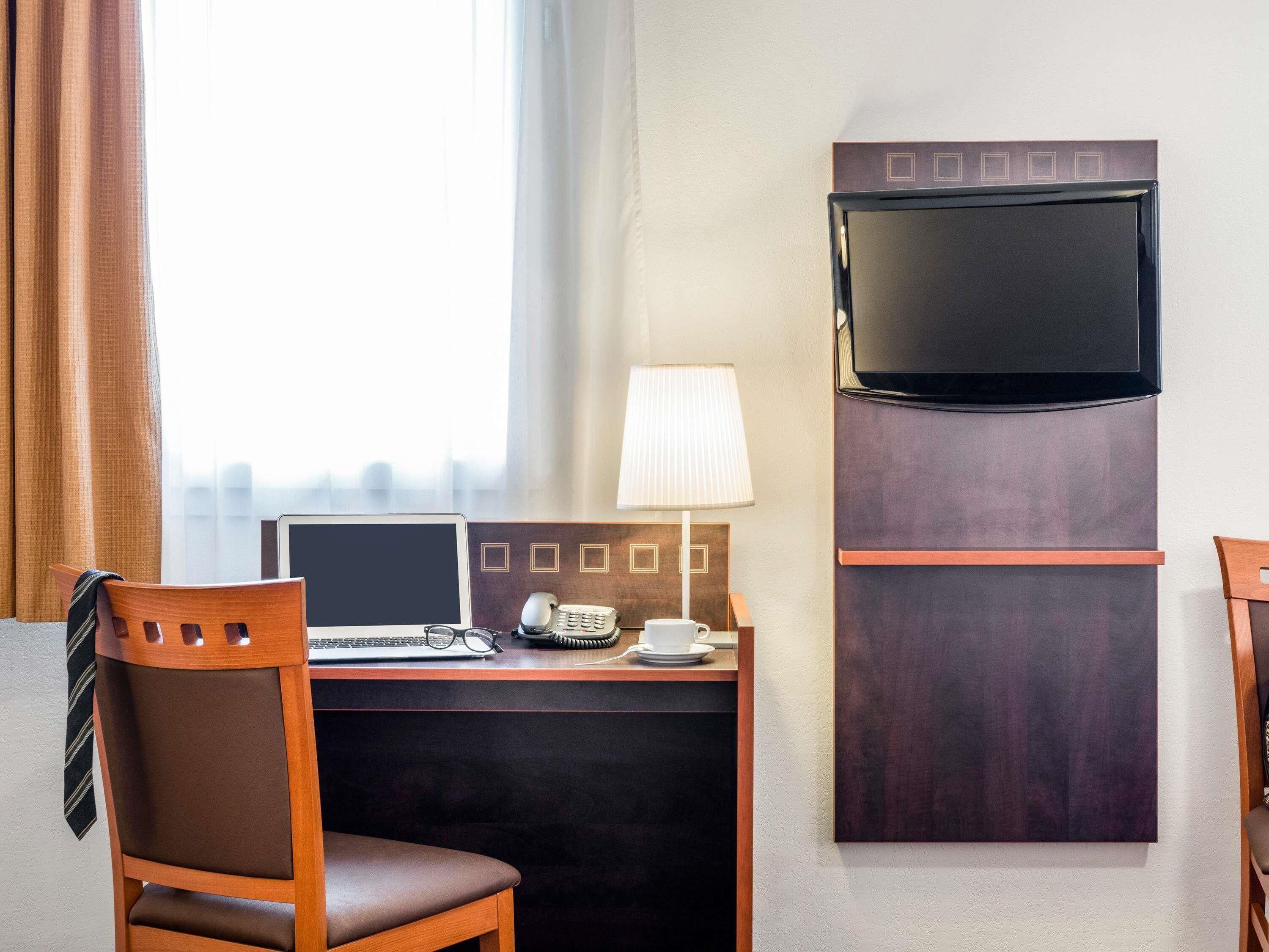 Ein Hotelzimmer mit Schreibtisch, Stuhl, Fernseher, Lampe und Blick auf die Stadt.