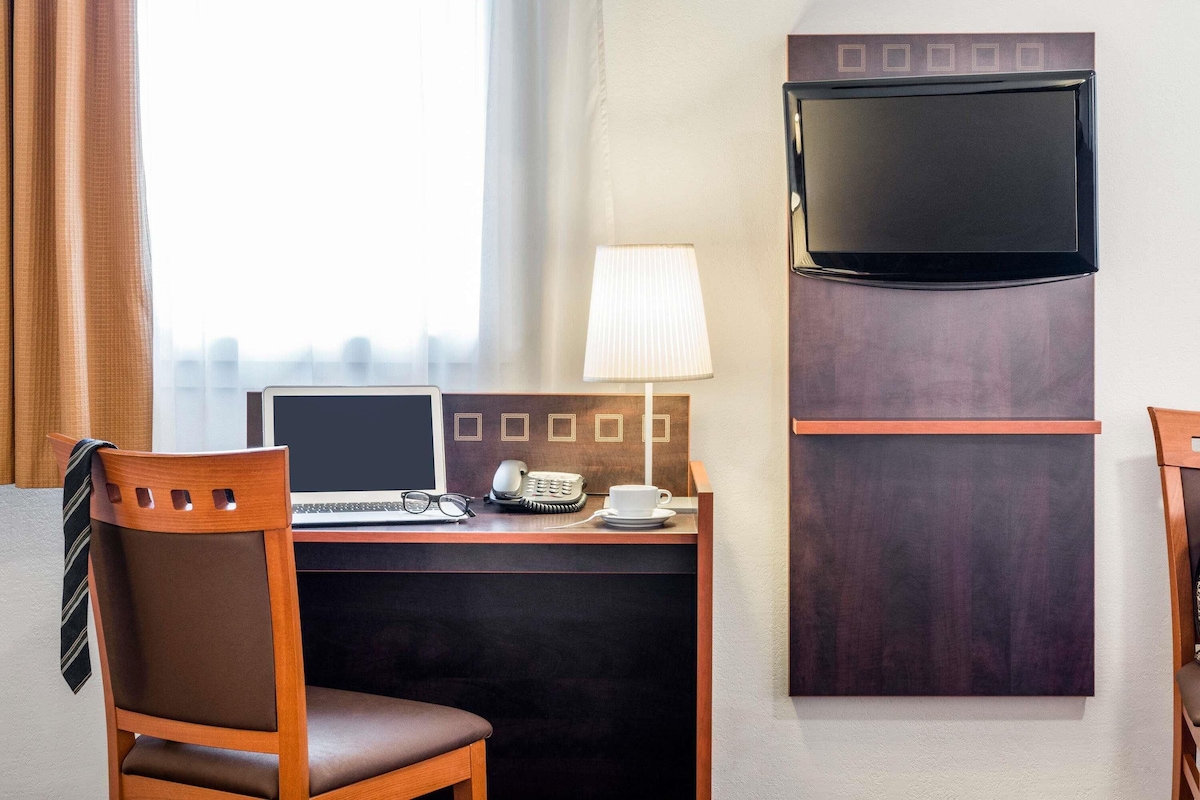 Hotellihuone, jossa on työpöytä, tuoli, televisio, lamppu ja näkymä kaupunkiin.