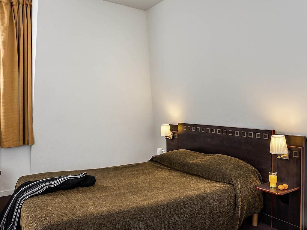 A hotel room with a single bed, a nightstand with a lamp, and a window with curtains.