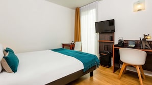 A hotel room with a bed, a desk with a computer, a TV, and a chair.
