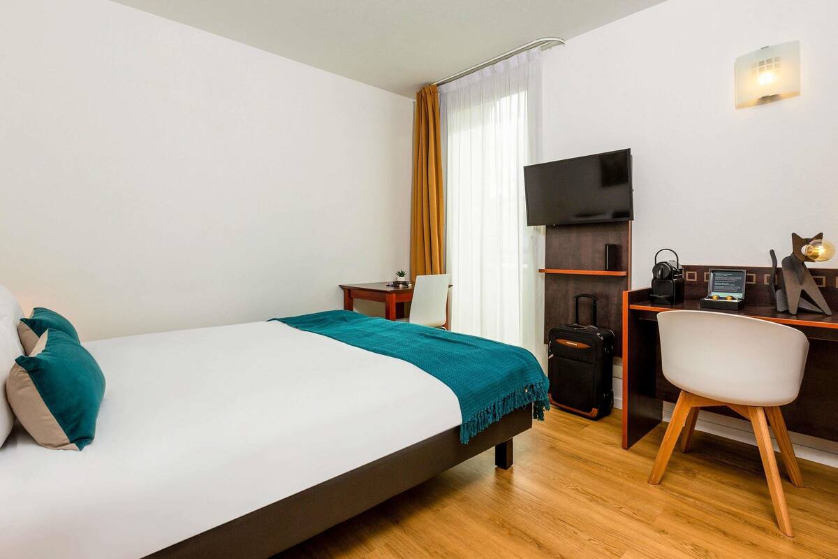Une chambre d’hôtel avec un lit, un bureau avec un ordinateur, une télévision et une chaise.