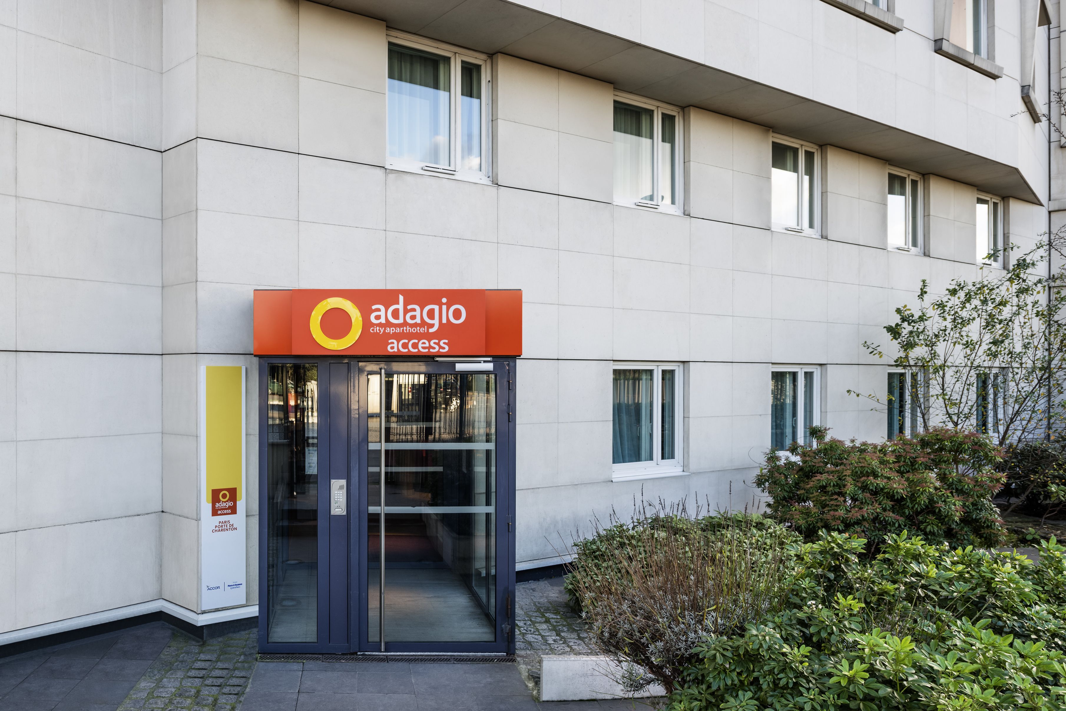 Un edificio moderno con puerta de entrada de cristal y un cartel que indica 'Adagio City Apartment Hotel Access'.