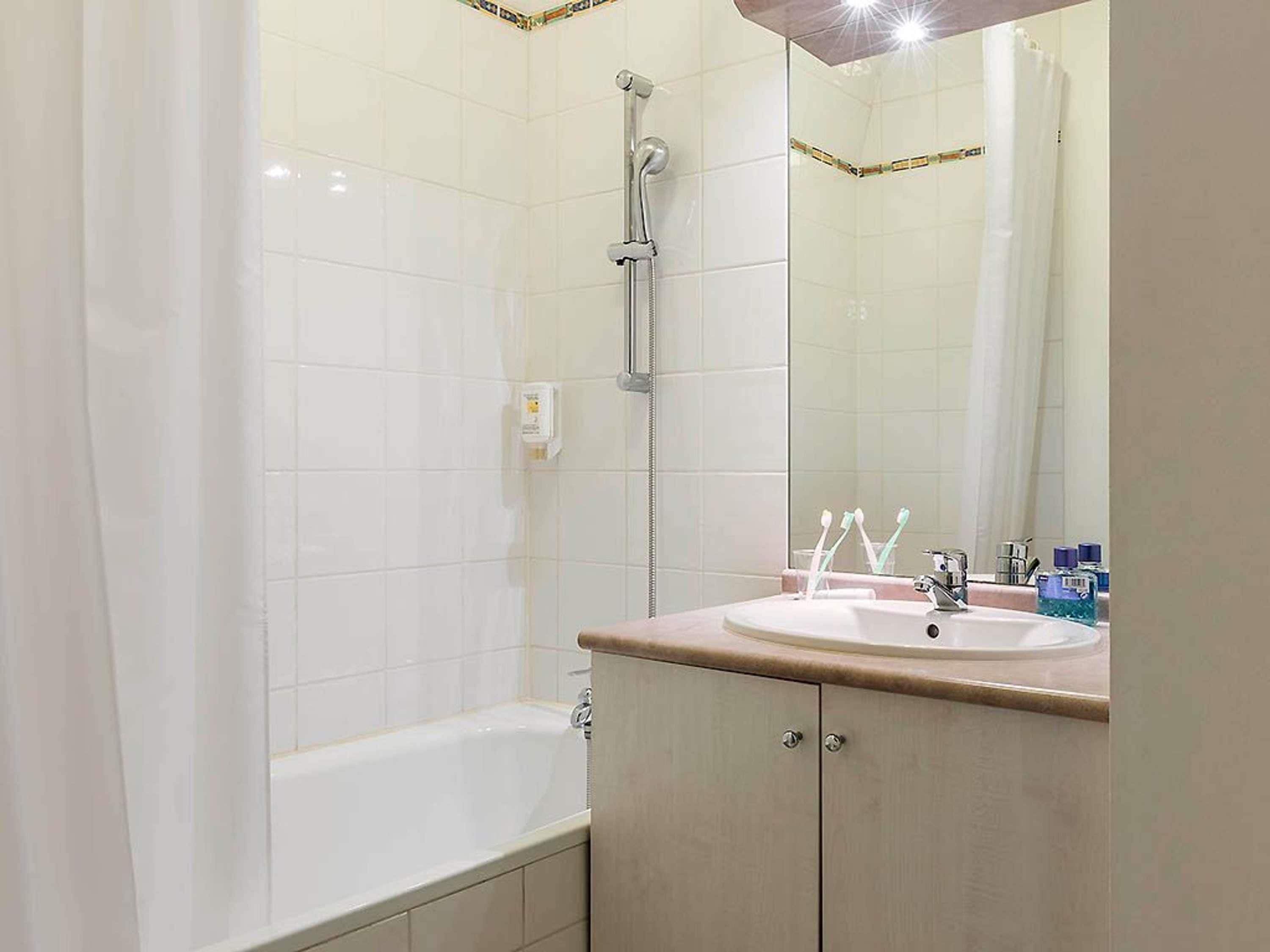 Une salle de bain équipée d’une baignoire, d’une douche, d’un lavabo avec des articles de toilette et d’un miroir.