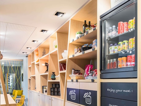 Un intérieur moderne avec des étagères en bois, un réfrigérateur rempli de boissons et un coin repas avec des chaises jaunes.. Aparthotel Adagio Access Paris Porte de Charenton