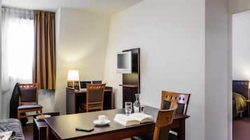 Une chambre d’hôtel équipée d’une table à manger, de chaises, d’un téléviseur, d’un lit et d’une fenêtre avec des rideaux.