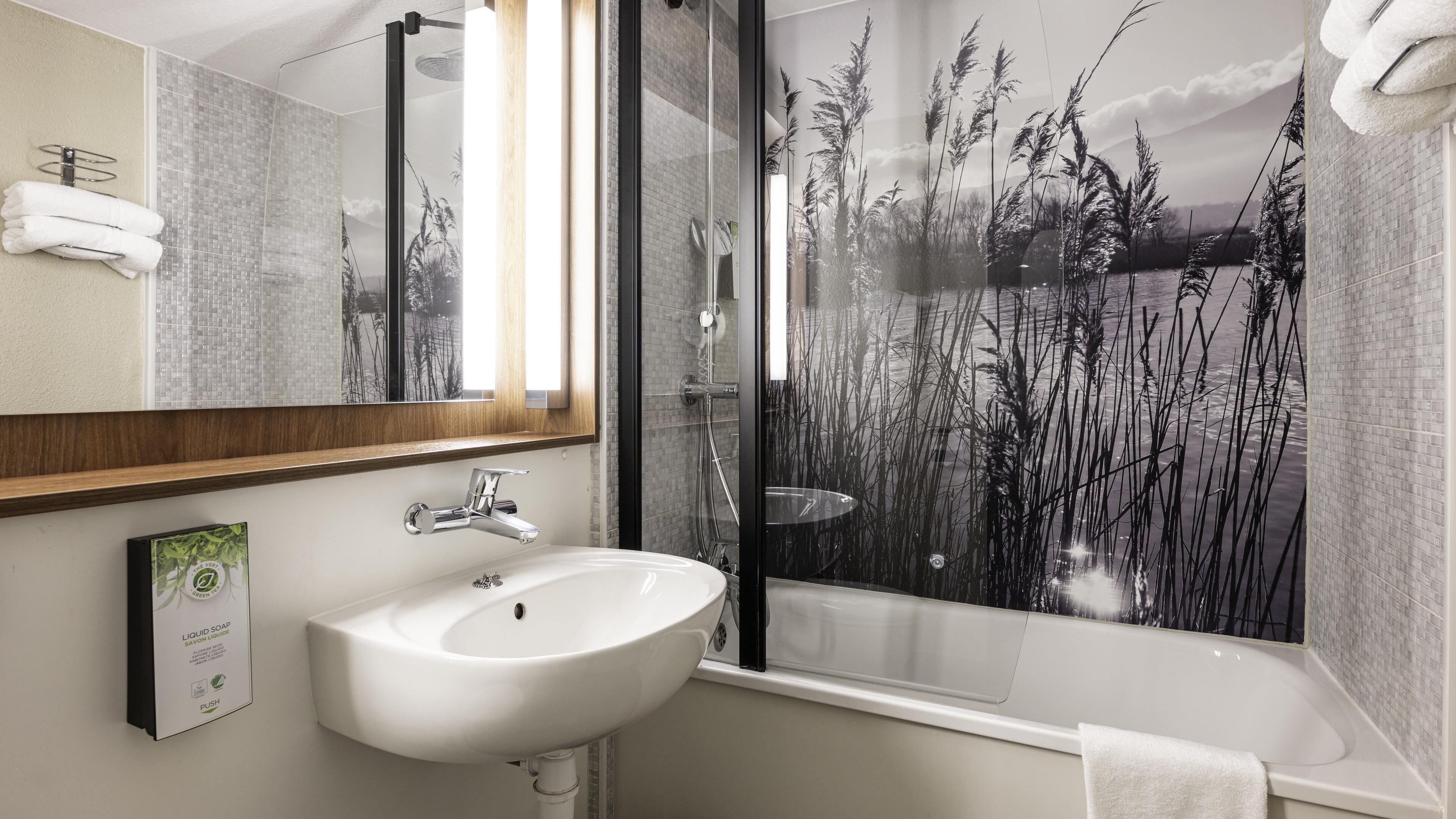 Un baño con lavamanos blanco, ducha con mampara de vidrio y un espejo grande.