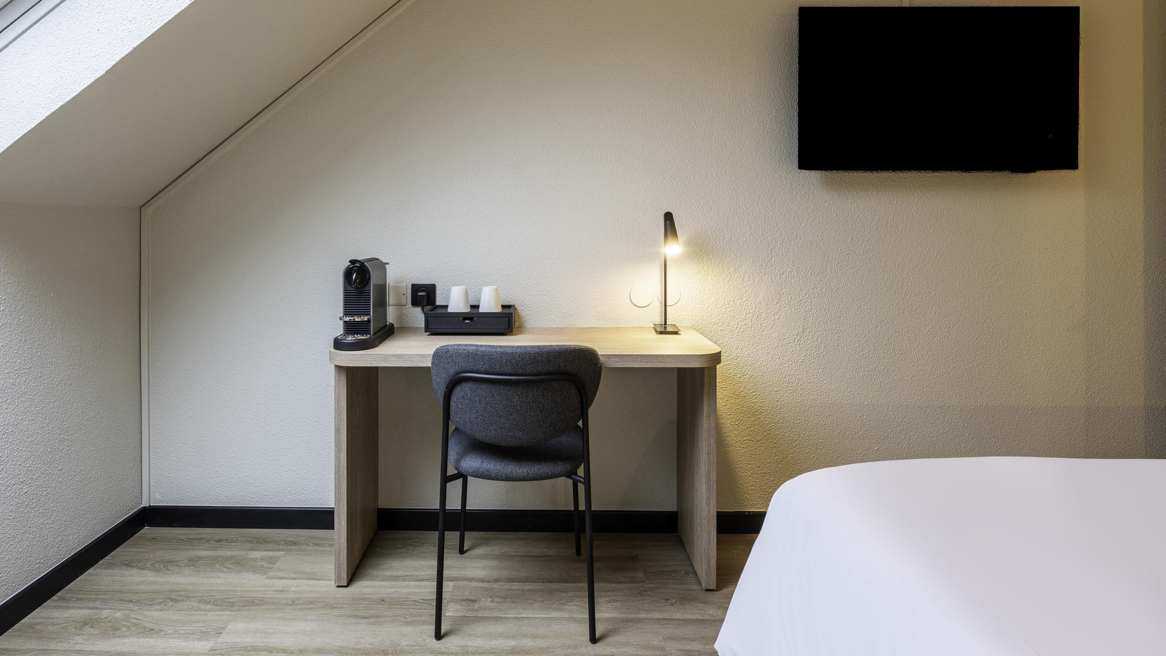 Een moderne hotelkamer met een bureau, stoel en een wandgemonteerde flatscreen-tv.