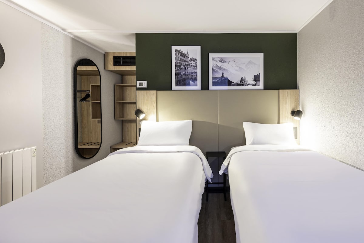 Ein Hotelzimmer mit zwei Einzelbetten, einem Holzschrank, einem Spiegel und zwei gerahmten Bildern an der Wand.