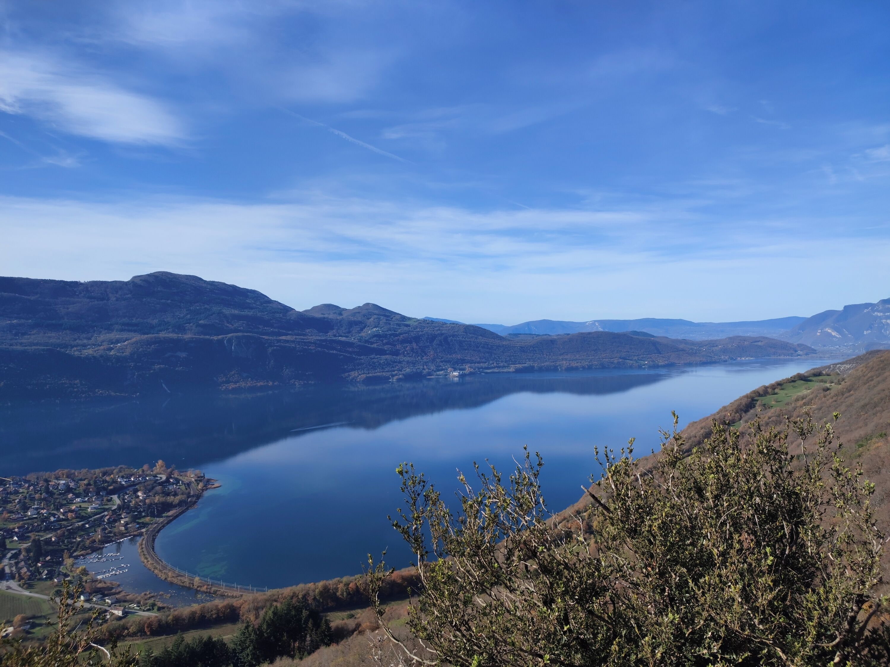 Una vista panorámica de un lago rodeado de colinas, con un pequeño pueblo visible a lo largo de la orilla.