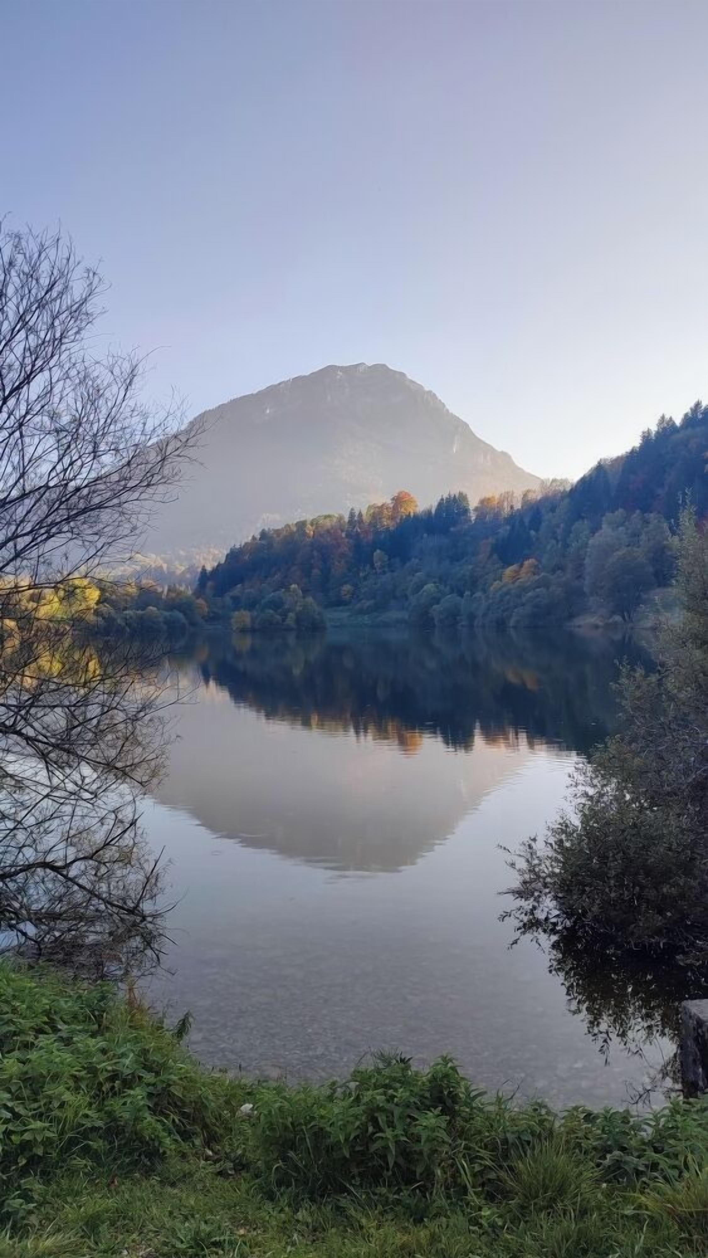 Um lago tranquilo com uma montanha ao fundo e uma floresta densa na margem oposta.