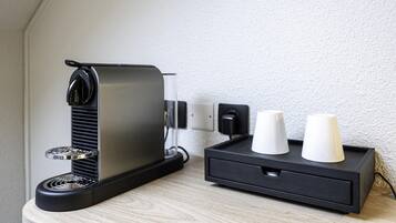 A coffee machine with a black base and a metallic top, placed on a wooden surface next to a black charging station with two white cups.