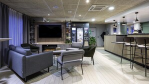 Una sala de estar moderna con televisor de pantalla plana, asientos cómodos, una barra de café y un mostrador de recepción.