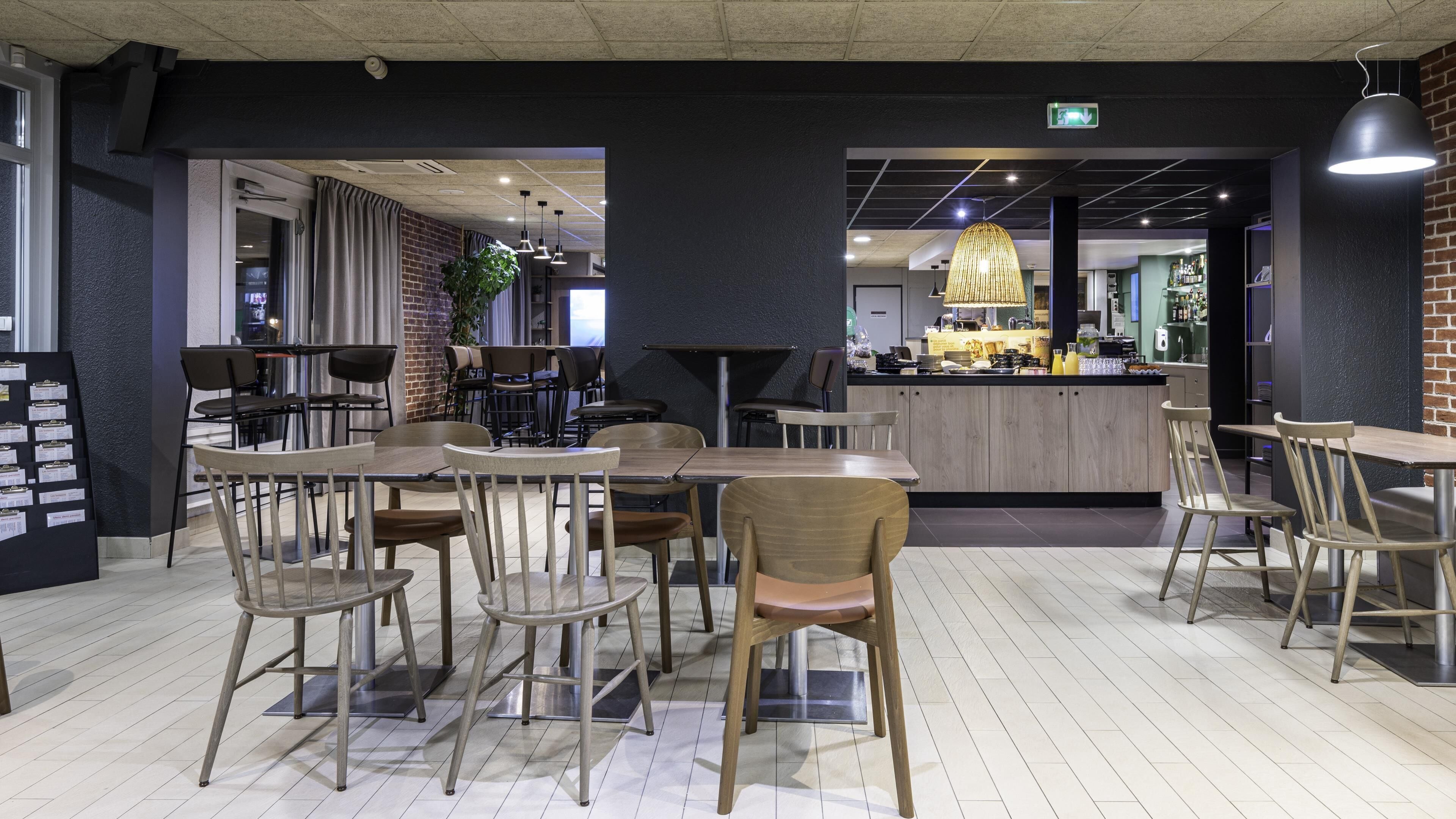 A modern restaurant with wooden tables and chairs, a bar area, and a brick wall.