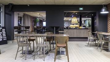 A modern restaurant with wooden tables and chairs, a bar area, and a brick wall.