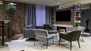 Una sala moderna con pared de ladrillo, sofá gris, sillones, un televisor de pantalla plana y una estantería.
