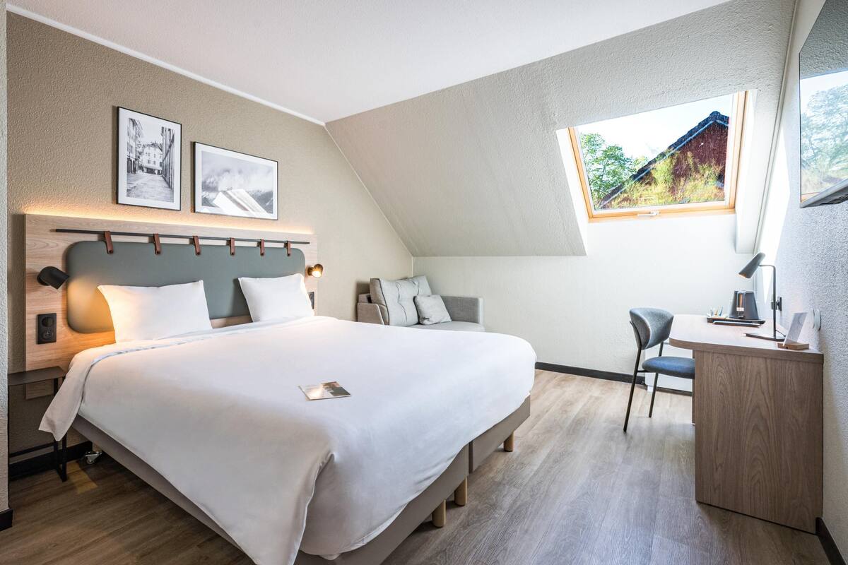 Ein modernes Hotelzimmer mit Bett, Schreibtisch und einem Fenster mit Blick.