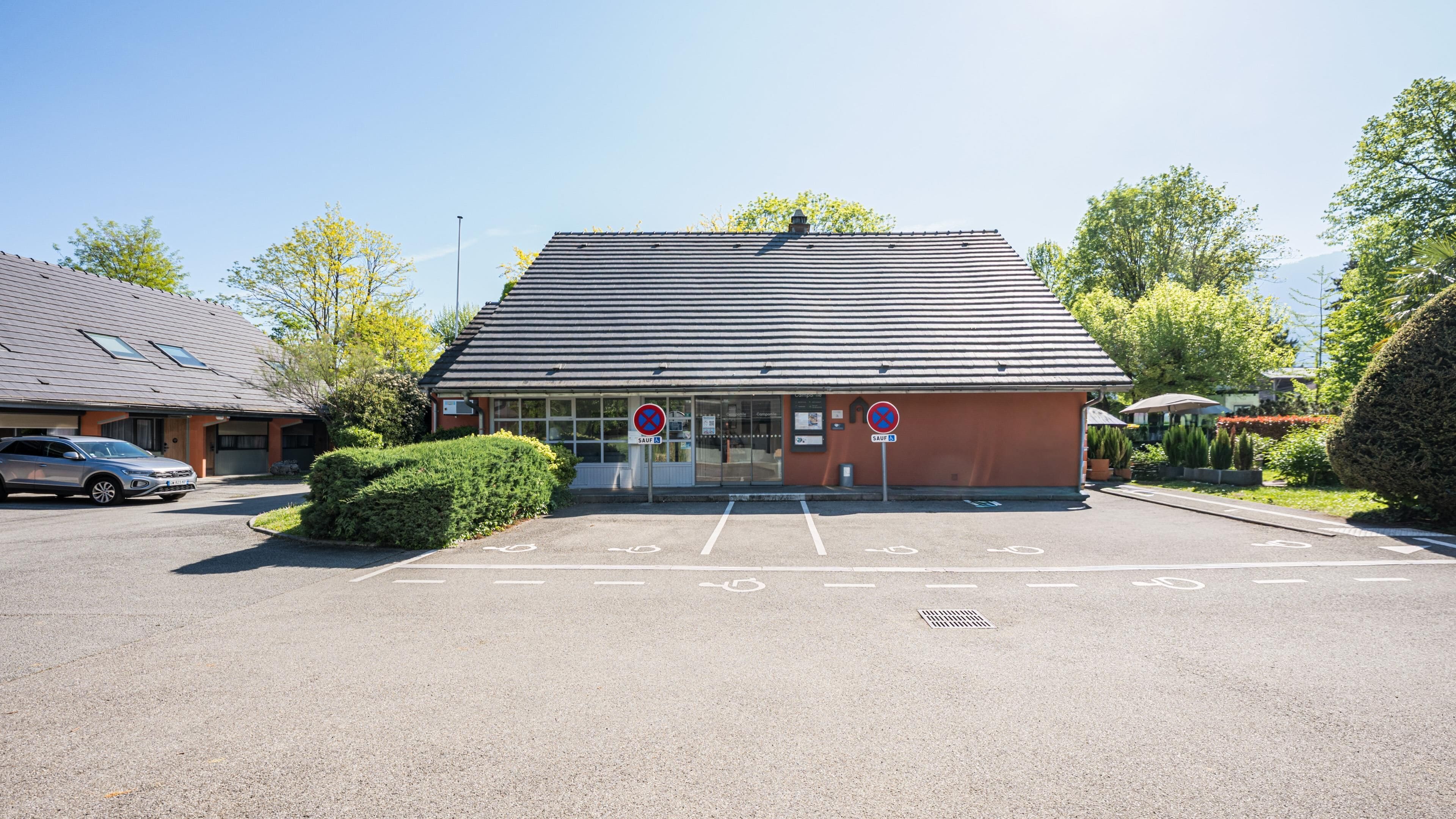 A building with a sloped roof, a parking lot with marked spaces, and two 'no parking' signs.
