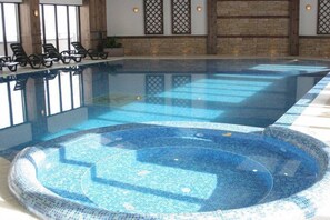 An indoor swimming pool with lounge chairs and a hot tub area.