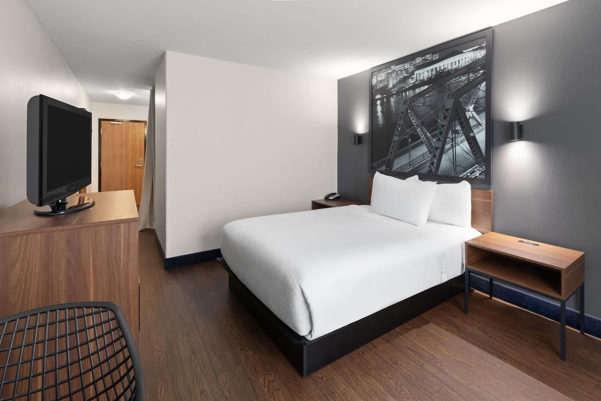 A modern hotel room with a large bed, a flat-screen TV, a desk, and a wall-mounted light.