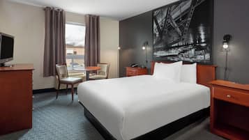 Una habitación de hotel con cama, escritorio, silla, lámpara y un ventanal con cortinas.