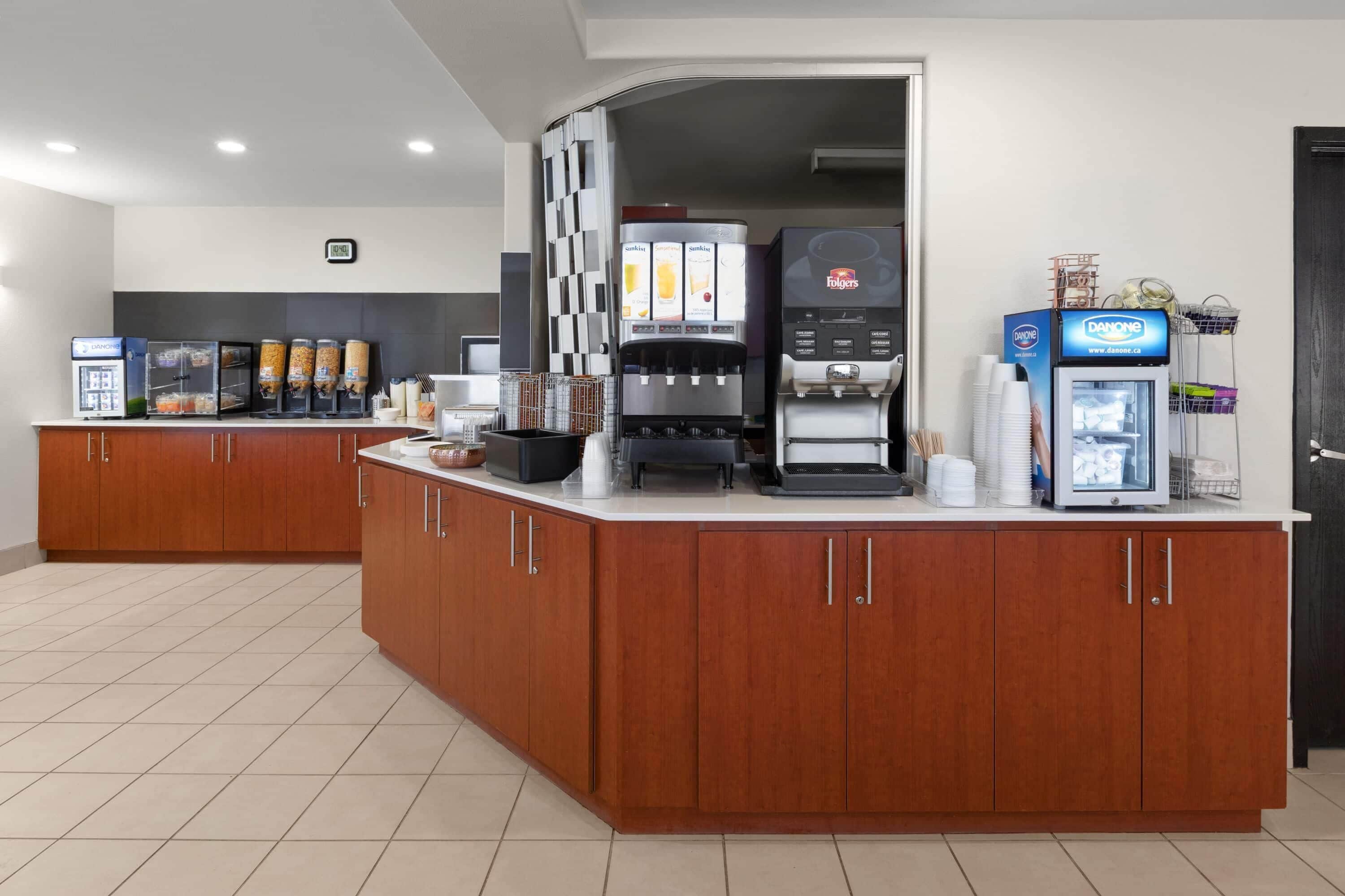 Een moderne keukenhoek met een koffiehoek, inclusief een koffieapparaat, een Danone-koelkast en een sapautomaat.