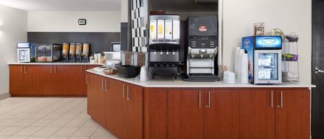 Een moderne keukenhoek met een koffiehoek, inclusief een koffieapparaat, een Danone-koelkast en een sapautomaat.