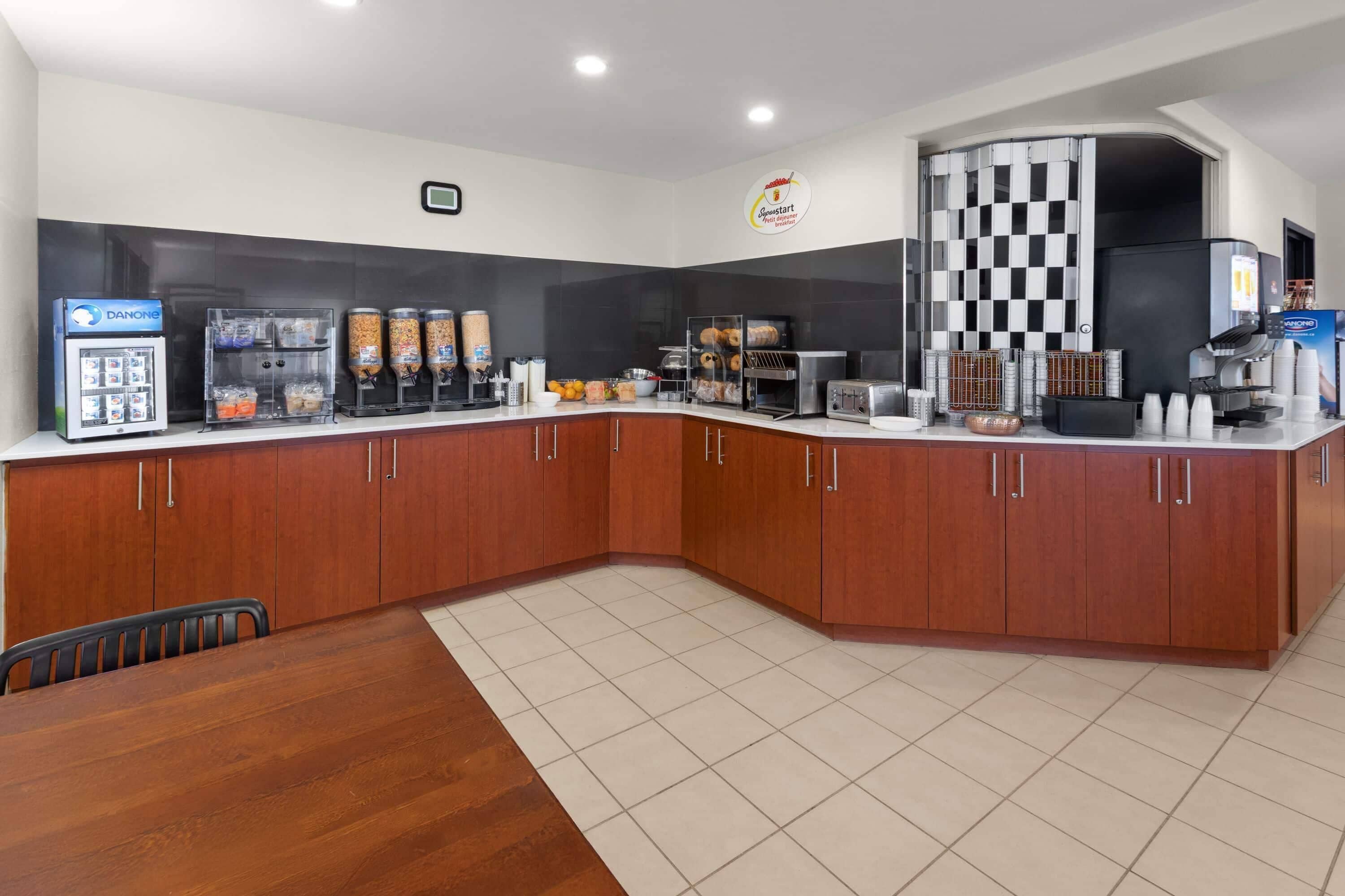 A modern kitchen with a checkered black and white wall, a Danone refrigerator, a coffee machine, and a microwave.