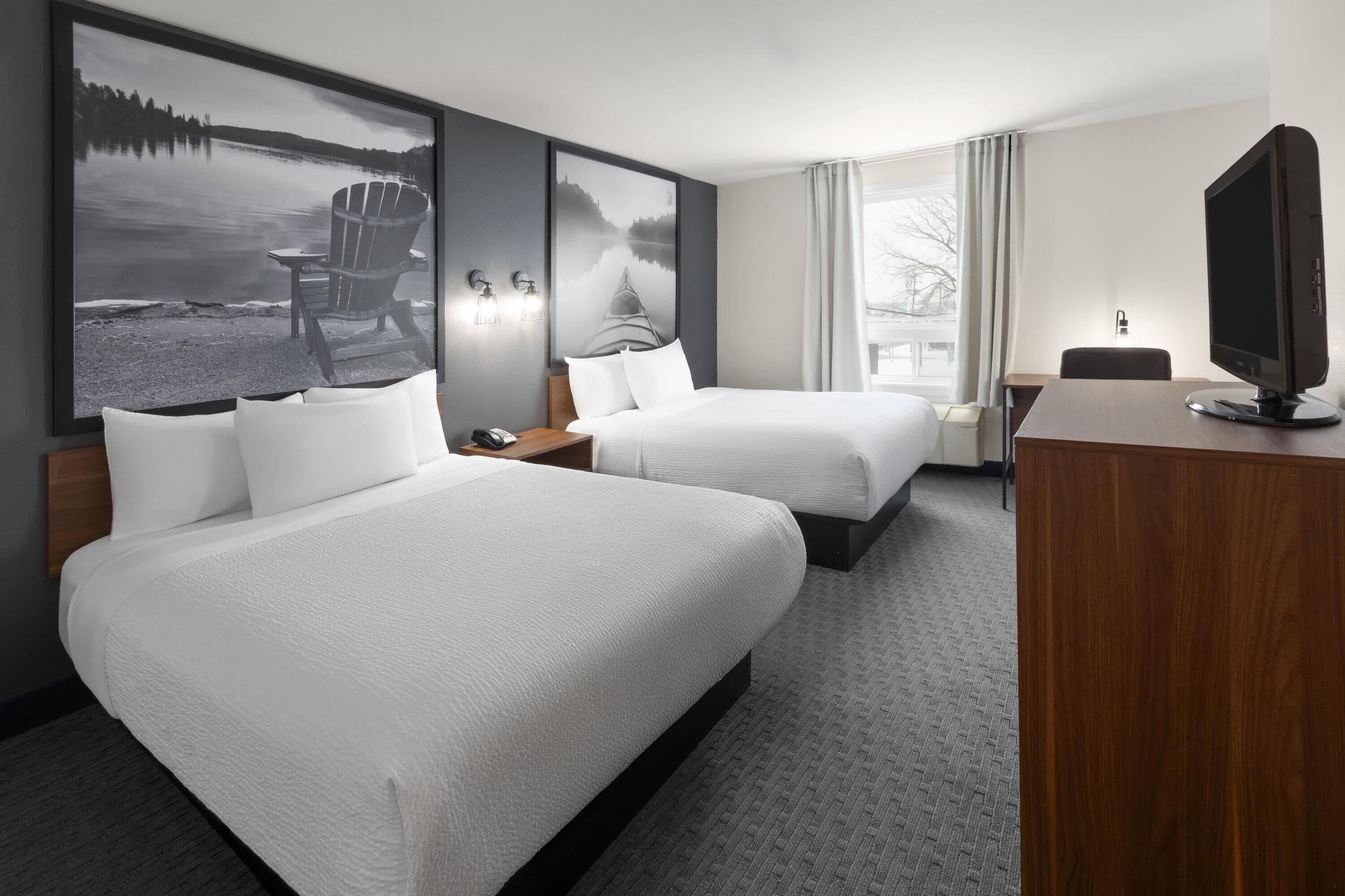 A hotel room with two beds, a desk, a television, and large landscape paintings on the walls.