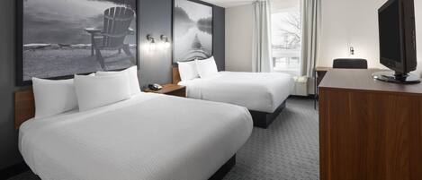 A hotel room with two beds, a desk, a television, and large landscape paintings on the walls.