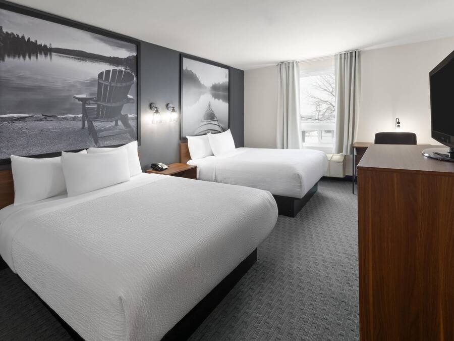 Una habitación de hotel con dos camas, un escritorio, un televisor y grandes cuadros con paisajes en las paredes.