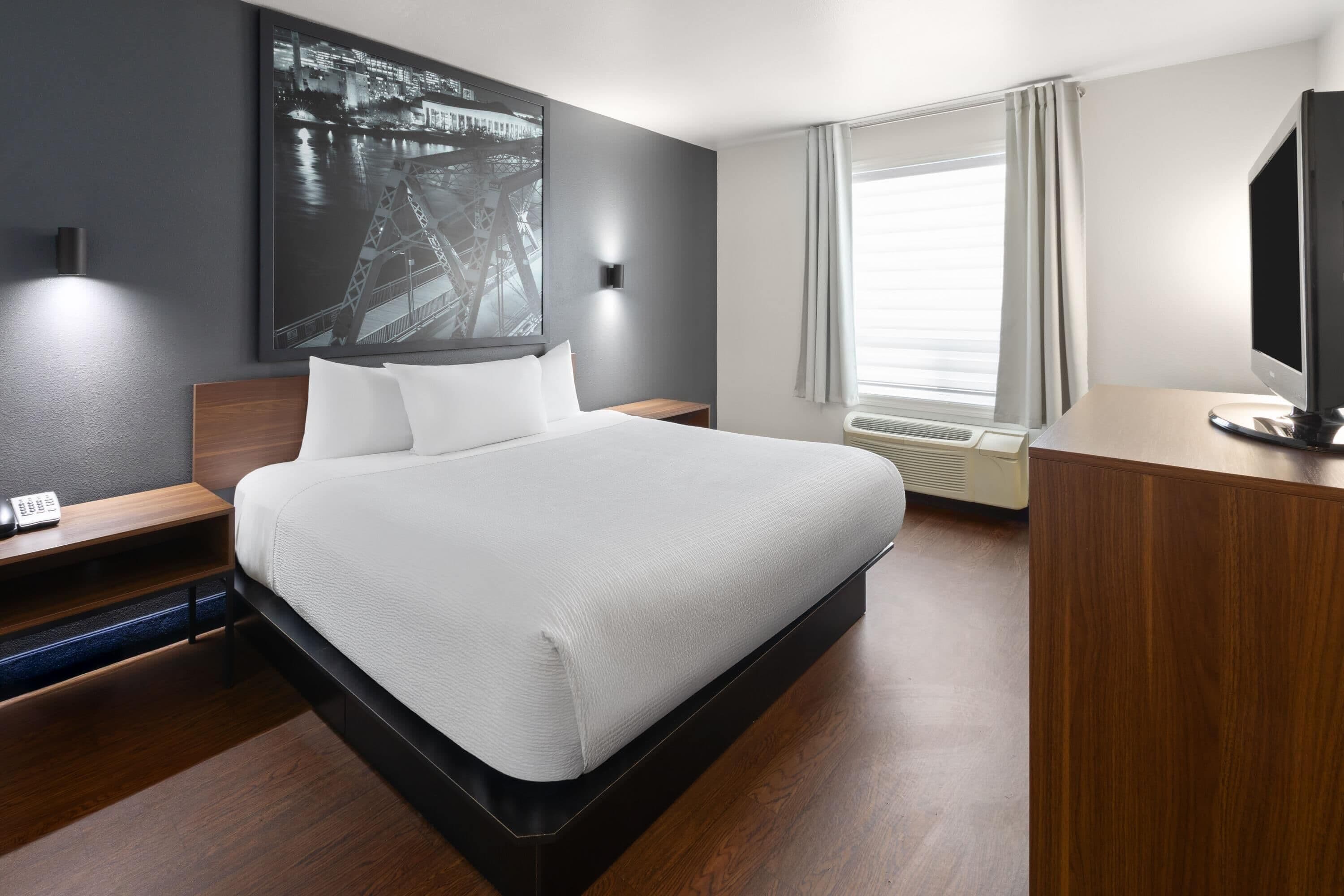 Een moderne hotelkamer met een groot bed, een bureau, een stoel, een televisie en een raam met gordijnen.