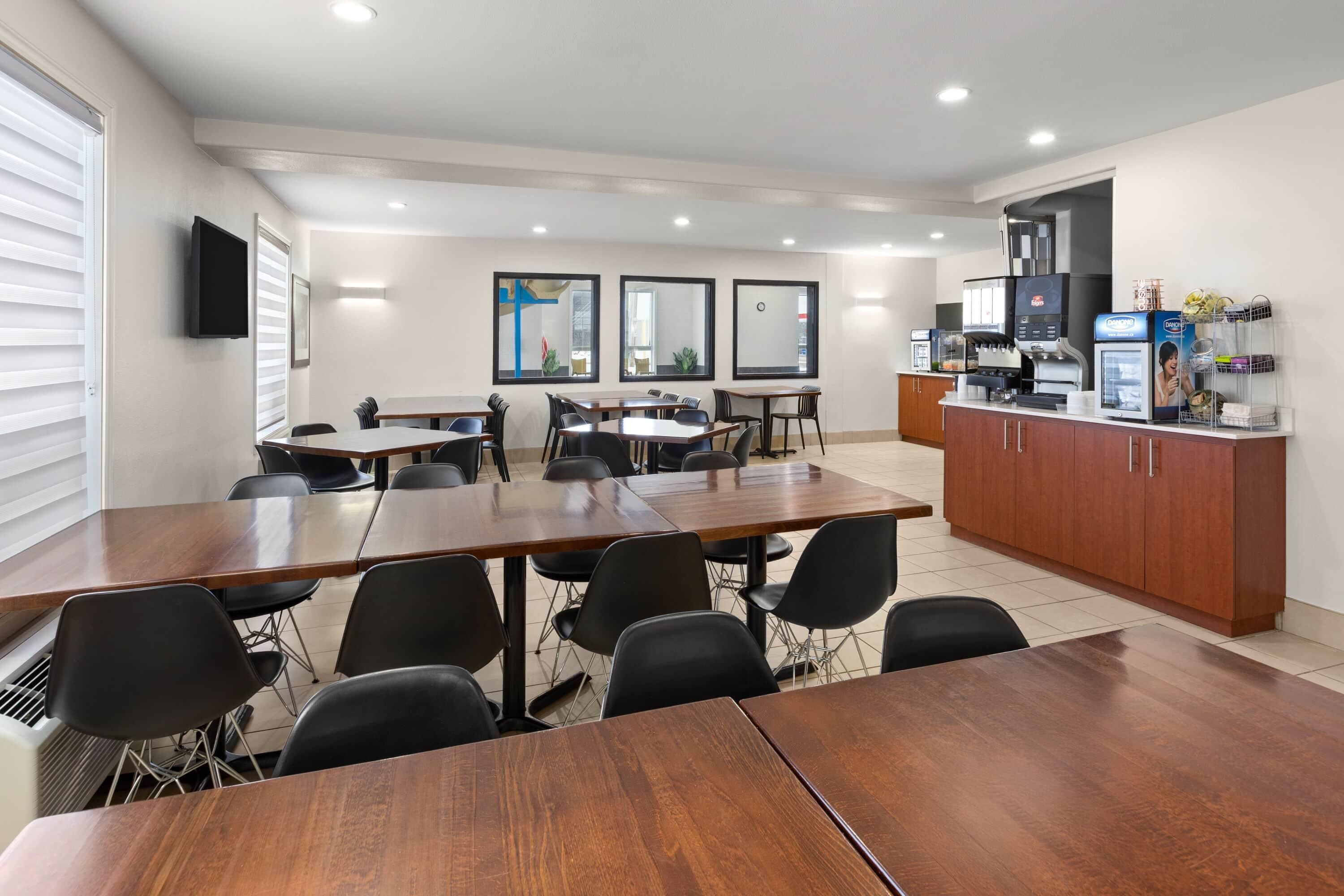 A conference room with a long table, multiple chairs, a coffee station, and a television mounted on the wall.