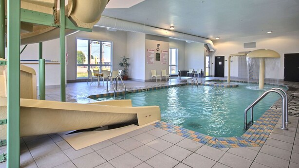 An indoor swimming pool with a slide, tiled floor, and clear glass walls.